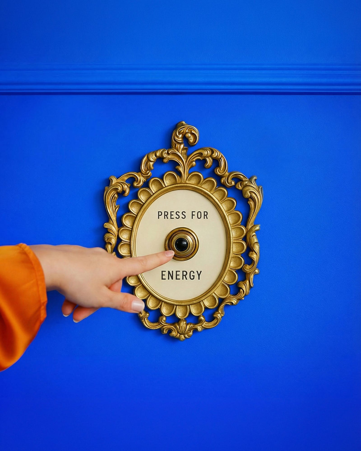 A hand pressing a gold Press for Energy bell on a blue wall